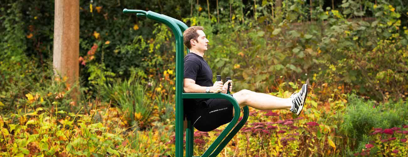 man using leg lift station outdoor gym equipment
