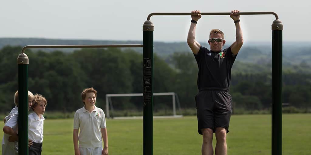 teacher doing pull ups with kids on outdoor gym 